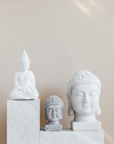 Set of various Marble and stone Buddha sculptures placed on white marble shelf against beige wall as home decoration element and religion symbol